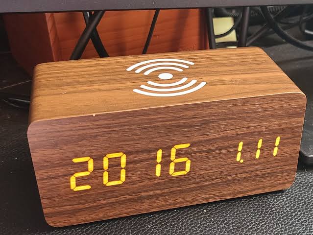 A wooden LED digital desk alarm clocks featuring Qi wireless charging pads built into their top surfaces